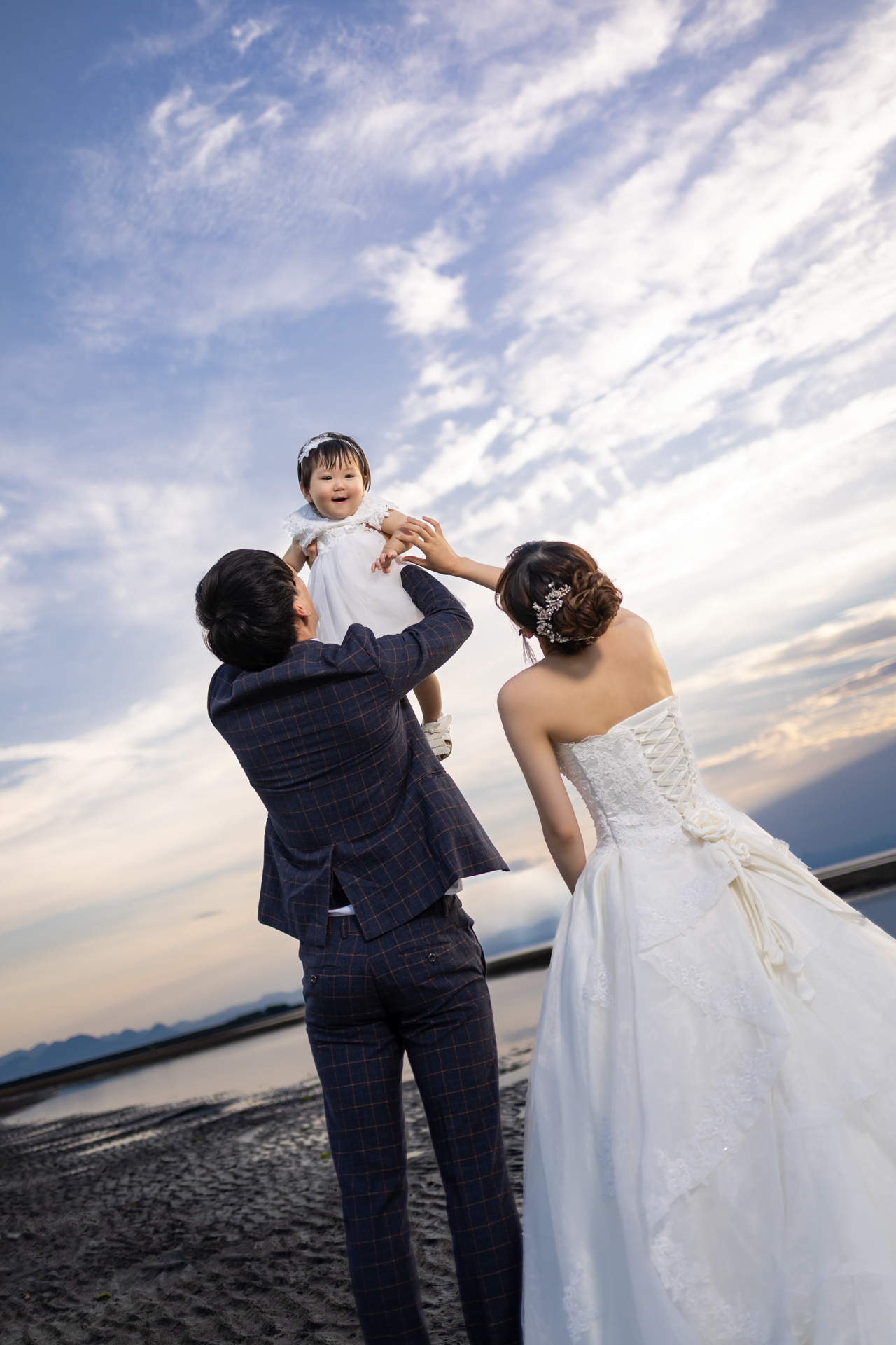 大分の海辺でお子様を高く抱き上げる感動的なパパママウエディング写真