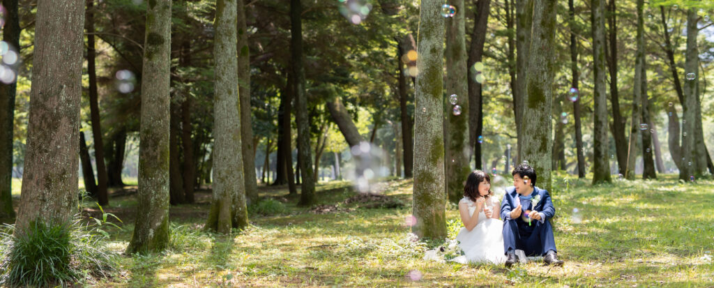 大分県別府市・別府公園のシロツメクサが広がる芝生で、笑顔で見つめ合う新郎新婦を撮影したフォトウェディングの一枚。