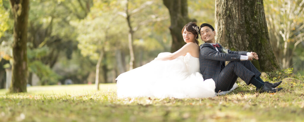 大分県別府市・別府公園でのドレス前撮り|芝生と木々を背景に座る新郎新婦のウェディングフォト