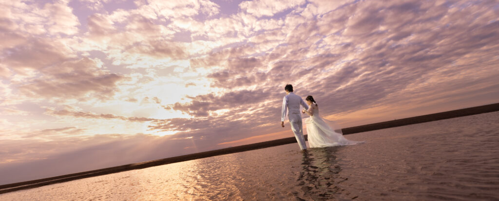 大分県豊後高田市・真玉海岸で撮影した、夕焼けと干潟を活かしたウェディングフォト。
茜色に染まる壮大な空と水面の反射の中を歩く二人を、ドラマチックに切り取った一枚です。