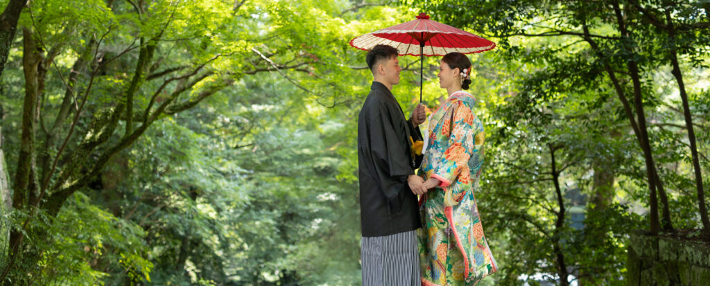 大分市の柞原八幡宮で和装前撮り。緑に囲まれた参道で、黒紋付の新郎と白無垢の新婦が手を取り合い、額を寄せ合う姿