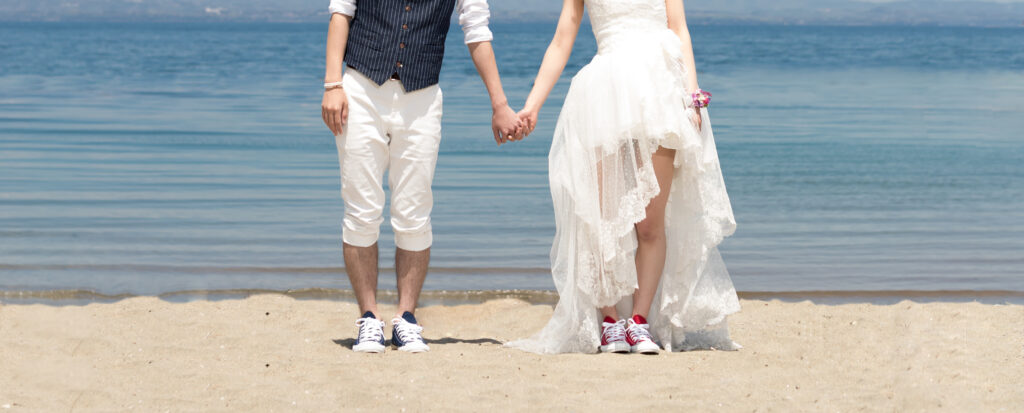 大分市・田ノ浦ビーチでフォトウェディング。穏やかな海を背景に、手をつなぐ新郎新婦とおそろいのスニーカーを写した一枚。