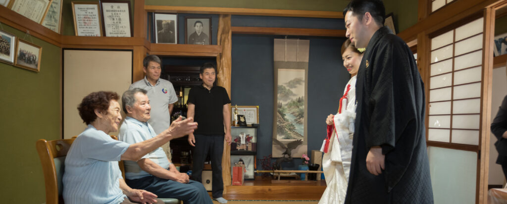 結婚式を前に祖父母へ晴れ姿を見せる新郎新婦と、笑顔で祝福する家族の温かなひととき