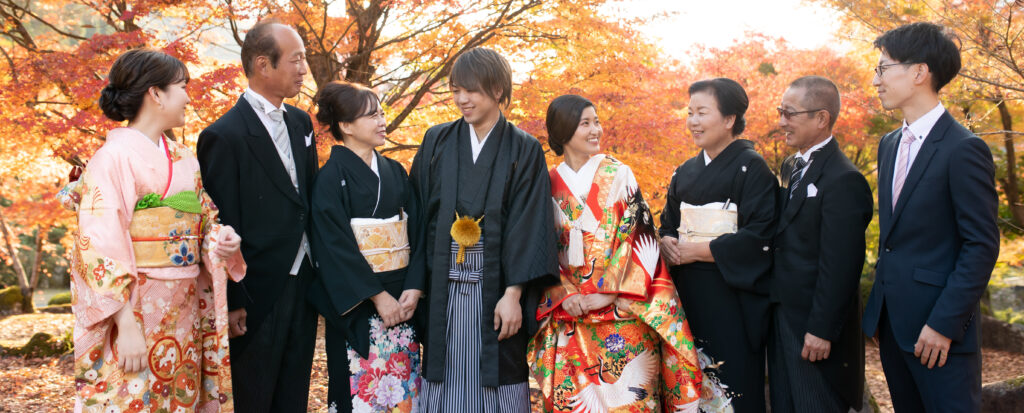 渓石園の色鮮やかな紅葉を背景に、和装の新郎新婦を両家の家族が囲んで笑顔を交わすフォトウェディング