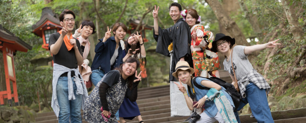 神社での和装前撮りを終え、黒紋付袴の新郎と色打掛の新婦が撮影スタッフと笑顔で記念撮影する様子