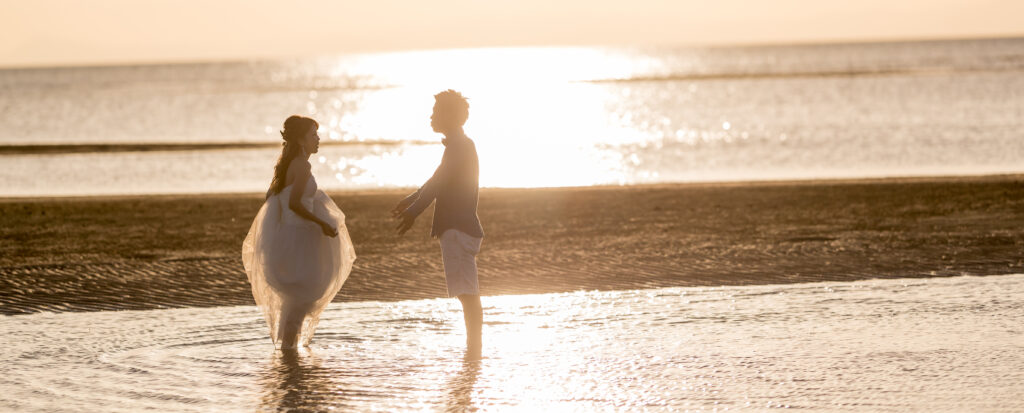 Photostudio PASSION夕日の輝く海辺で、水辺に立って向かい合う新郎新婦をシルエットで撮影したフォトウェディング